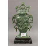 A green jade lidded vase decorated with a dragon and a pierced wooden stand. 35 cm high overall.