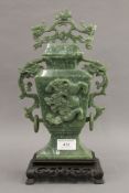 A green jade lidded vase decorated with a dragon and a pierced wooden stand. 35 cm high overall.