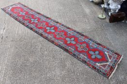 A red ground wool runner. 85 x 490 cm.