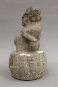 An early Chinese carved stone temple dog sitting on a drum with paw resting on a ball. 33 cm high.