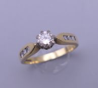 An 18 ct gold diamond solitaire ring, with diamond set shoulders. The central stone approximately 0.