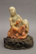 A Chinese carved soapstone model of a bearded figure holding a cup, mounted on a carved plinth base.