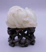 A Chinese mutton fat jade carving on a wooden stand, formed as fruit and a bat. 5 cm high overall.