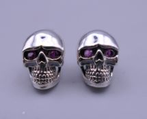 A pair of silver skull earrings. Each 1 cm high.