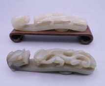 Two Chinese carved jade dragon form belt hooks, one mounted on a carved wooden plinth.