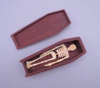 A wood and bone skeleton in a coffin. 12 cm long.