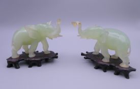 A pair of carved jade elephants, each mounted on a carved wooden stand. Each 10 cm long.