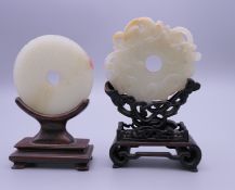 Two Chinese carved jade roundels, each mounted on a carved wooden stand. The largest 9.