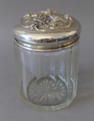 A cut glass powder jar, the sterling silver lid embossed with cherubs. 14.5 cm high.
