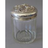 A cut glass powder jar, the sterling silver lid embossed with cherubs. 14.5 cm high.