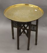 An Eastern folding table with engraved brass tray top, together with an additional base. 62.