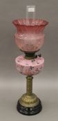 A brass column oil lamp with floral pink font and red etched shade. 66 cm high overall.