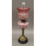 A brass column oil lamp with floral pink font and red etched shade. 66 cm high overall.