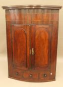 A Georgian mahogany bowfront hanging corner cupboard. 121 cm high.