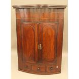 A Georgian mahogany bowfront hanging corner cupboard. 121 cm high.