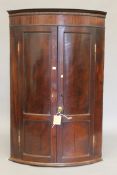 A Georgian mahogany bowfront hanging corner cupboard. 113.5 cm high.