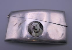 A silver card case decorated with a dog's head roundel,