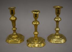 An 18th century brass candlestick on a canted corner base and two other brass candlesticks.