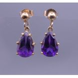 A pair of unmarked gold amethyst drop earrings. 1.5 cm high.