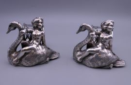 A pair of silver plated napkin rings, each surmounted with a putto riding a swan. 7 cm wide.