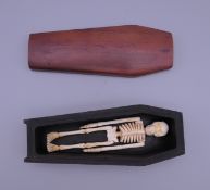 A miniature wooden coffin containing a bone skeleton. 12.5 cm long.