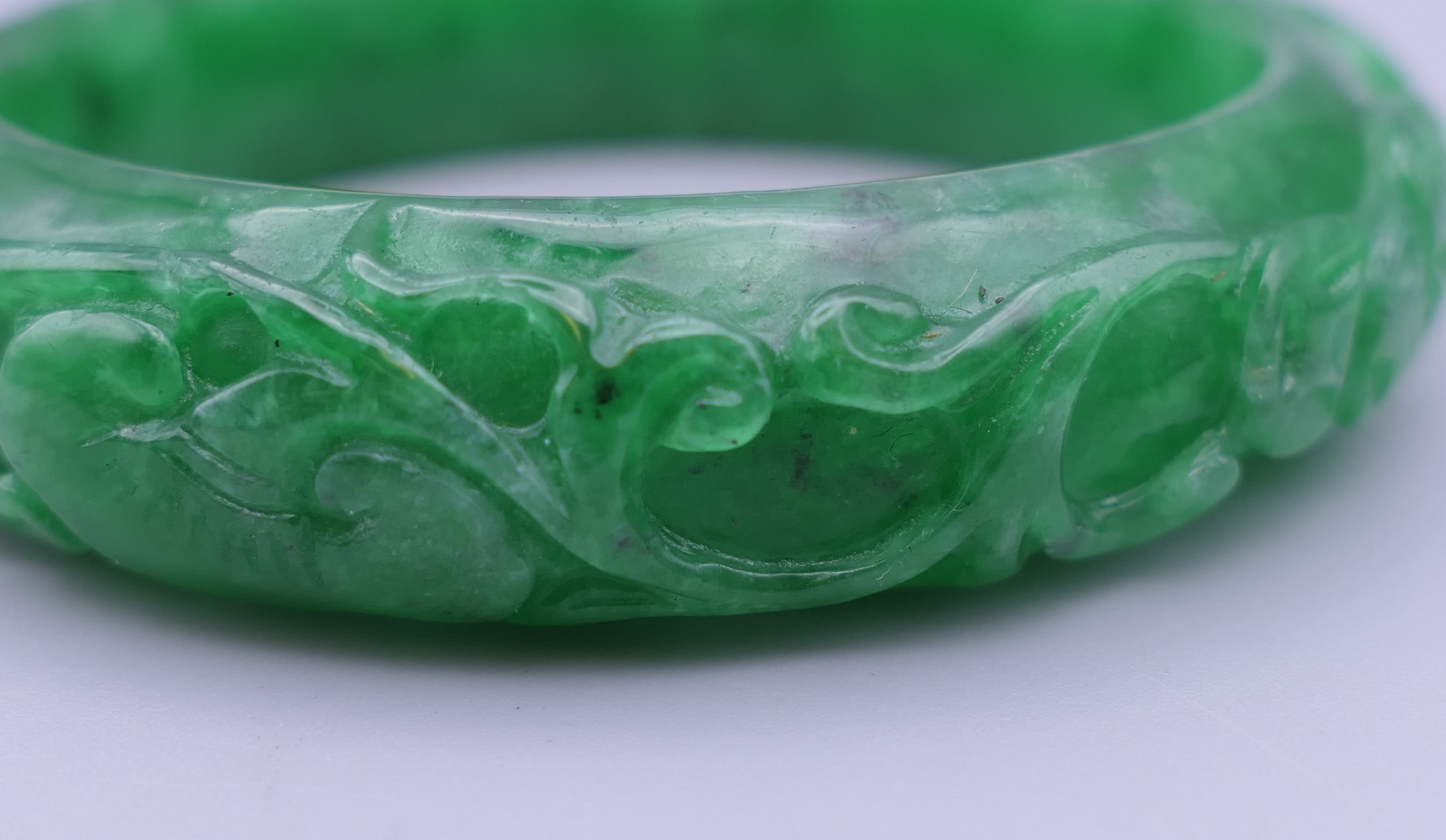 A carved apple green jade bangle. 7 cm outer diameter, 5.5 cm inner diameter. - Image 2 of 3
