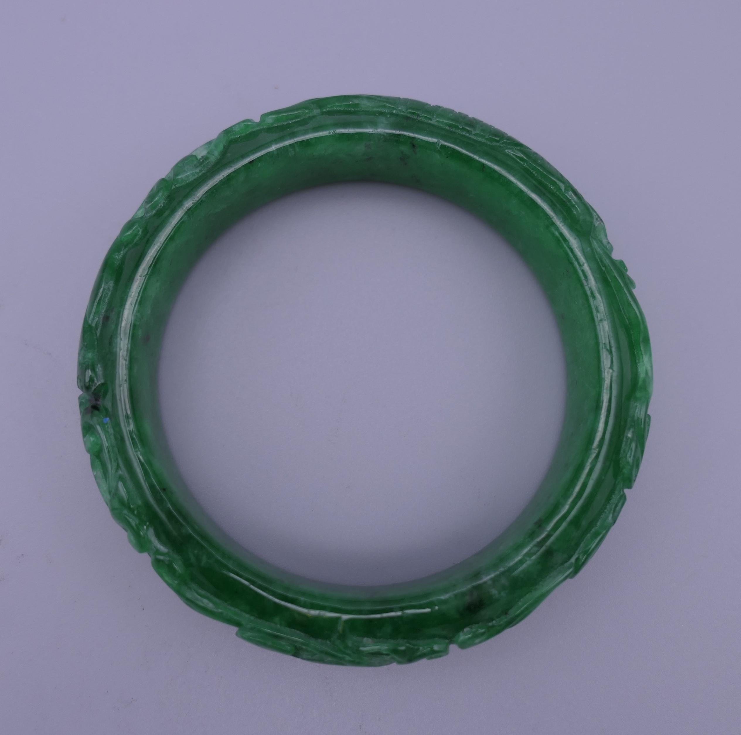 A carved apple green jade bangle. 7 cm outer diameter, 5.5 cm inner diameter. - Image 3 of 3