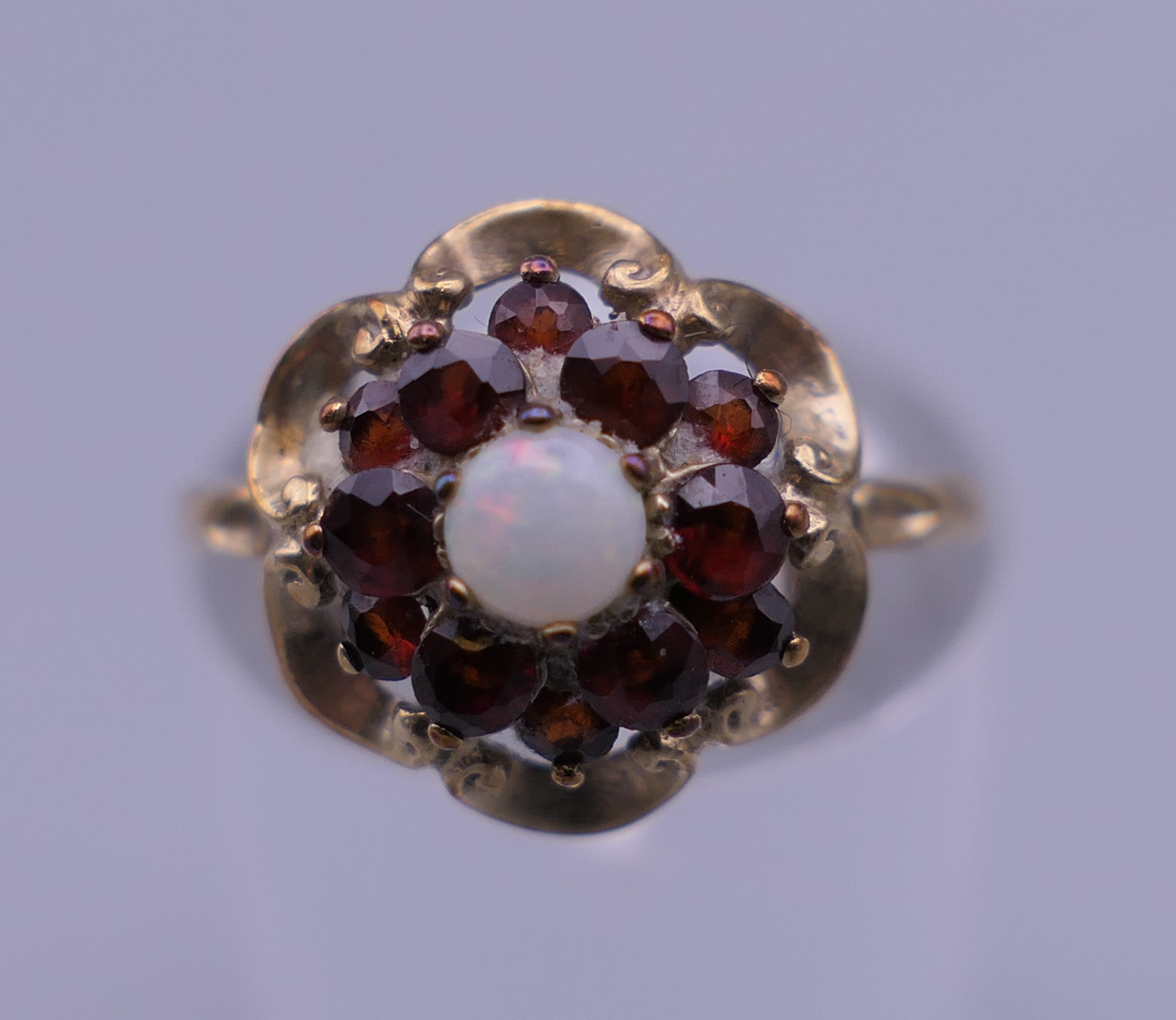 An unmarked 9 ct gold garnet and opal ring. Ring size M. 1.6 grammes total weight.