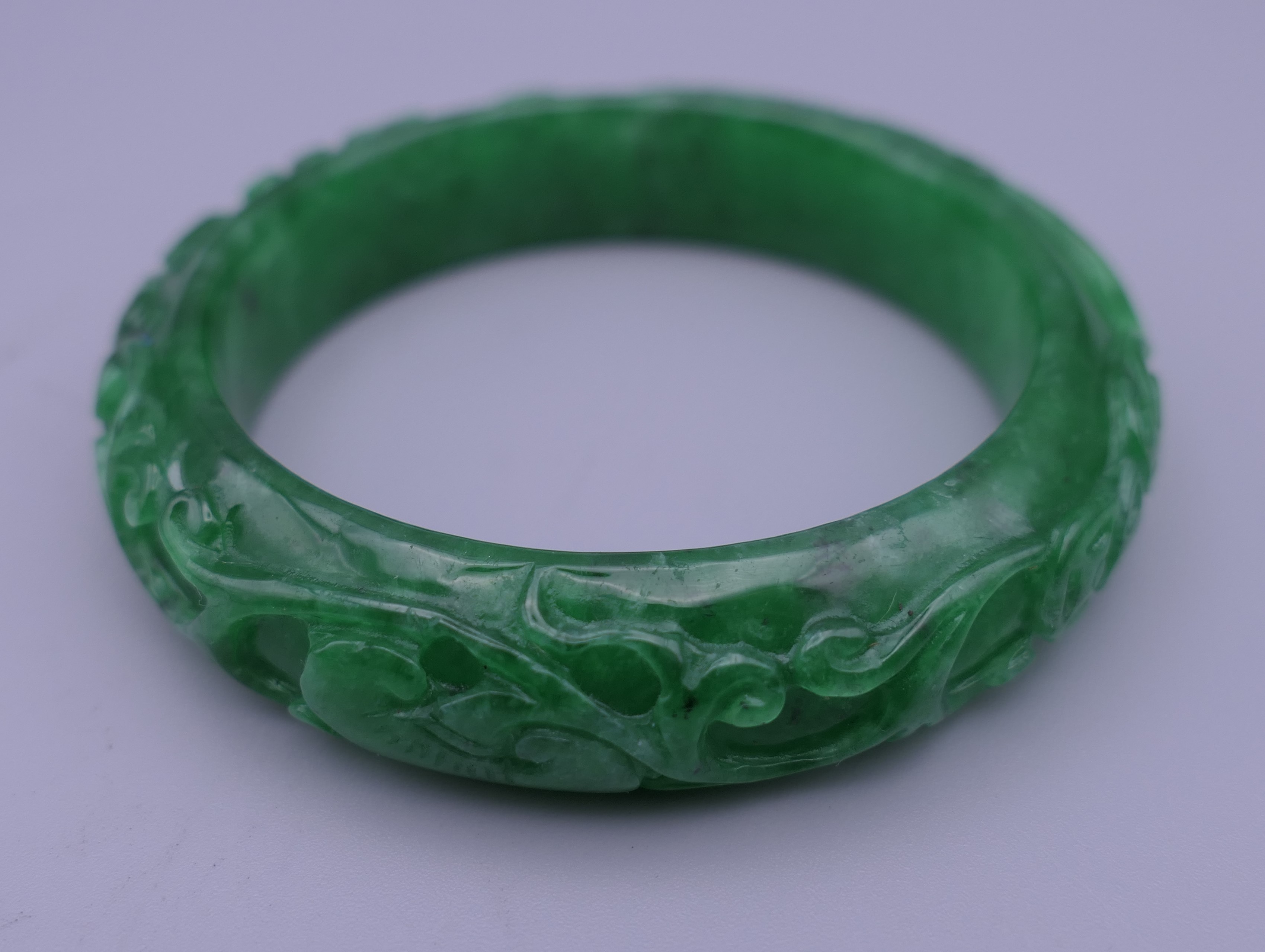 A carved apple green jade bangle. 7 cm outer diameter, 5.5 cm inner diameter.