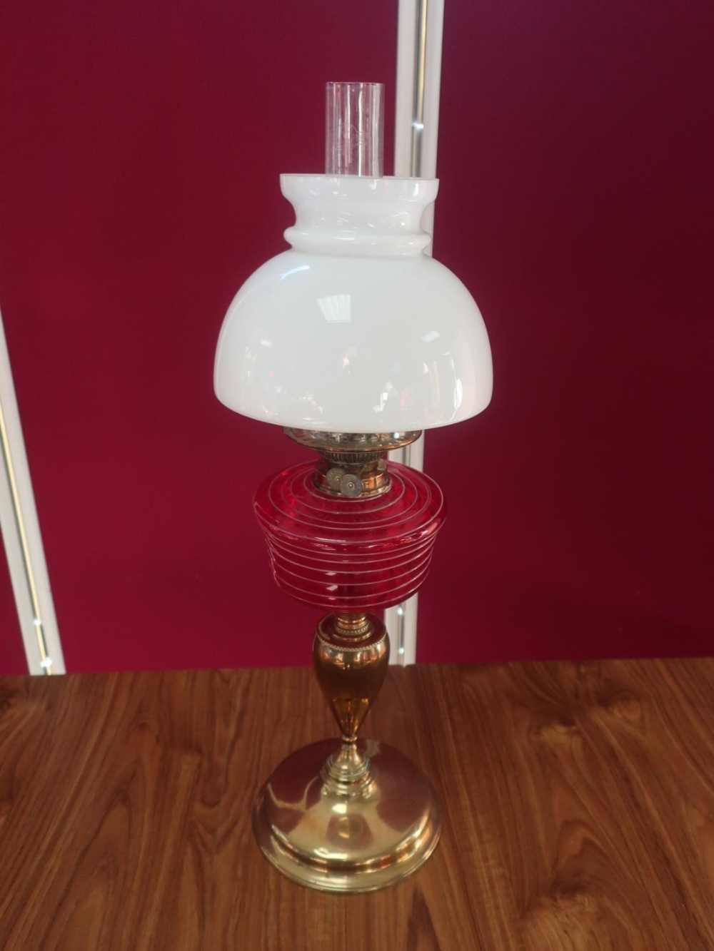 Early 20th C brass oil lamp, with red glass reservoir and clear glass shade, on urn shaped column