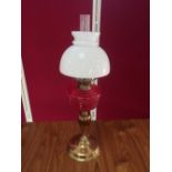 Early 20th C brass oil lamp, with red glass reservoir and clear glass shade, on urn shaped column