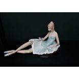 Porcelain figure depicting a resting ballerina holding a flower, H25cm L45cm.