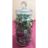 Confectioners glass storage jar containing a selection of marbles of different designs and sizes