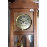 A 1920s golden oak wall clock, glazed panel door enclosing silver dial set with Arabic numerals, two