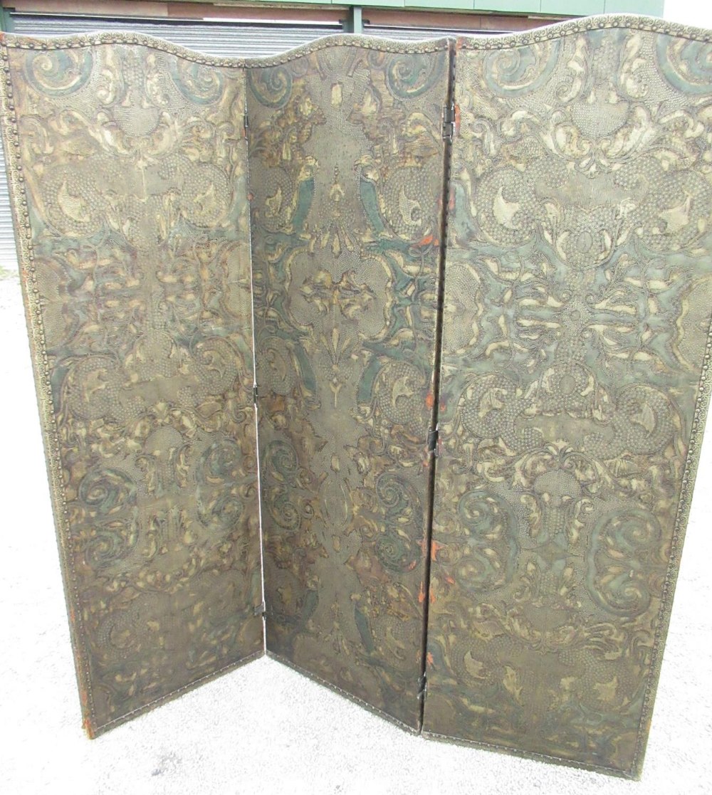 Early C20th two fold screen, the three arched panels with brass nailed embossed and painted