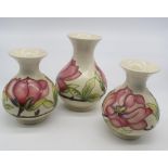 Garniture of three Moorcroft baluster vases decorated pink foliage and branch work on an ivory