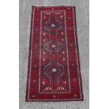 A Belouch woollen hand-made rug with red ground, 88 by 40ins. (224 by 102cms.).