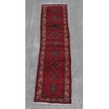 A Hamadan woollen hand-made runner with dark red ground, 121 by 31ins. (307 by 79cms.).