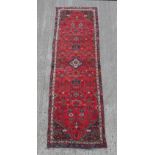 A Hamadan woollen hand-made runner with red ground, 112 by 34ins. (285 by 87cms.).