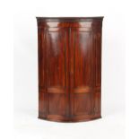 Property of a gentleman - a George III mahogany bow-fronted panelled two-door corner wall cabinet