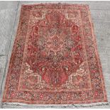 A Heriz woollen hand-made carpet with red ground, 126 by 89ins. (325 by 225cms.).
