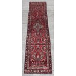 A Hamadan woollen hand-made runner with red ground, 150 by 37ins. (380 by 94cms.).