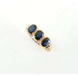 An unmarked yellow gold sapphire three stone ring, the three rub over set oval cut sapphires