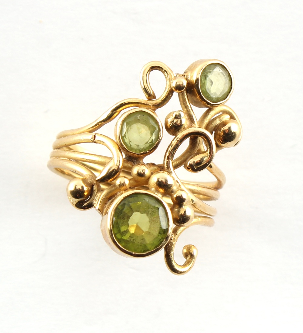 A modern 18ct yellow gold stylised scrolling foliate ring set with three round cut peridots, size Q,