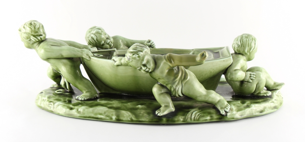 A Clement Massier green glazed centrepiece modelled as four putti hauling a rowing boat,