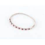 An 18ct white gold ruby & diamond hinged bangle, set with nine round cut rubies alternating with