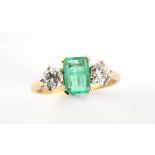 An unmarked yellow gold emerald & diamond three stone ring, the central rectangular cut emerald