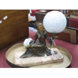 An Art Deco Table Lamp, as a lady seated, supporting the white mottle globe shade on her hand, on