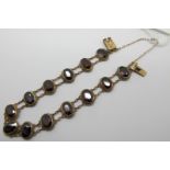 A Garnet Set Bracelet, composed of thirteen oval collet set garnets, on two row fine chain