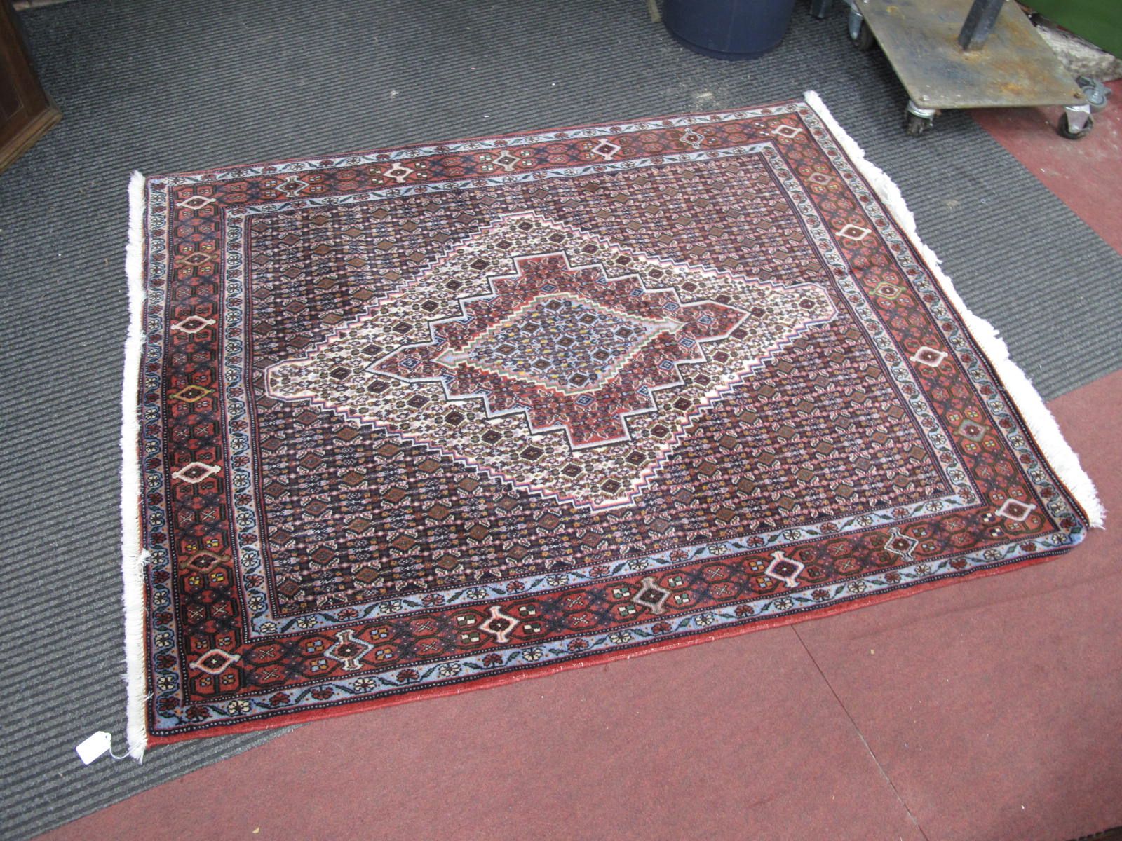 A Middle Eastern Wool Tasselled Rug, with allover geometric motifs, diamond shapes to centre, on red